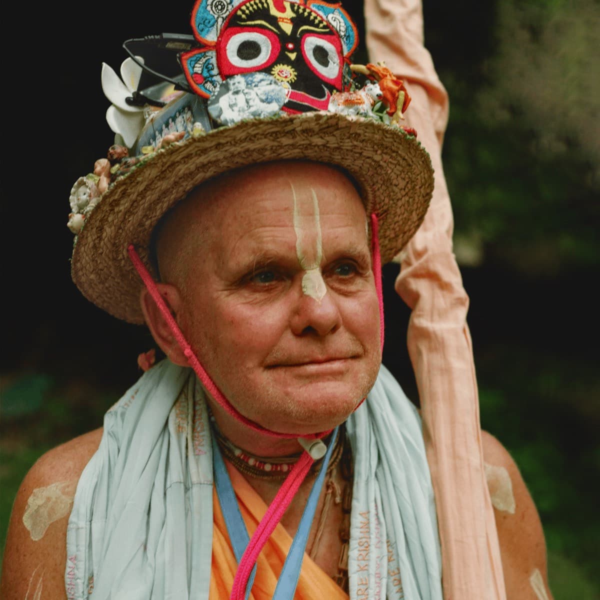 Mahavishnu Swami wearing a colourful straw hat decorated with a Jagannath face